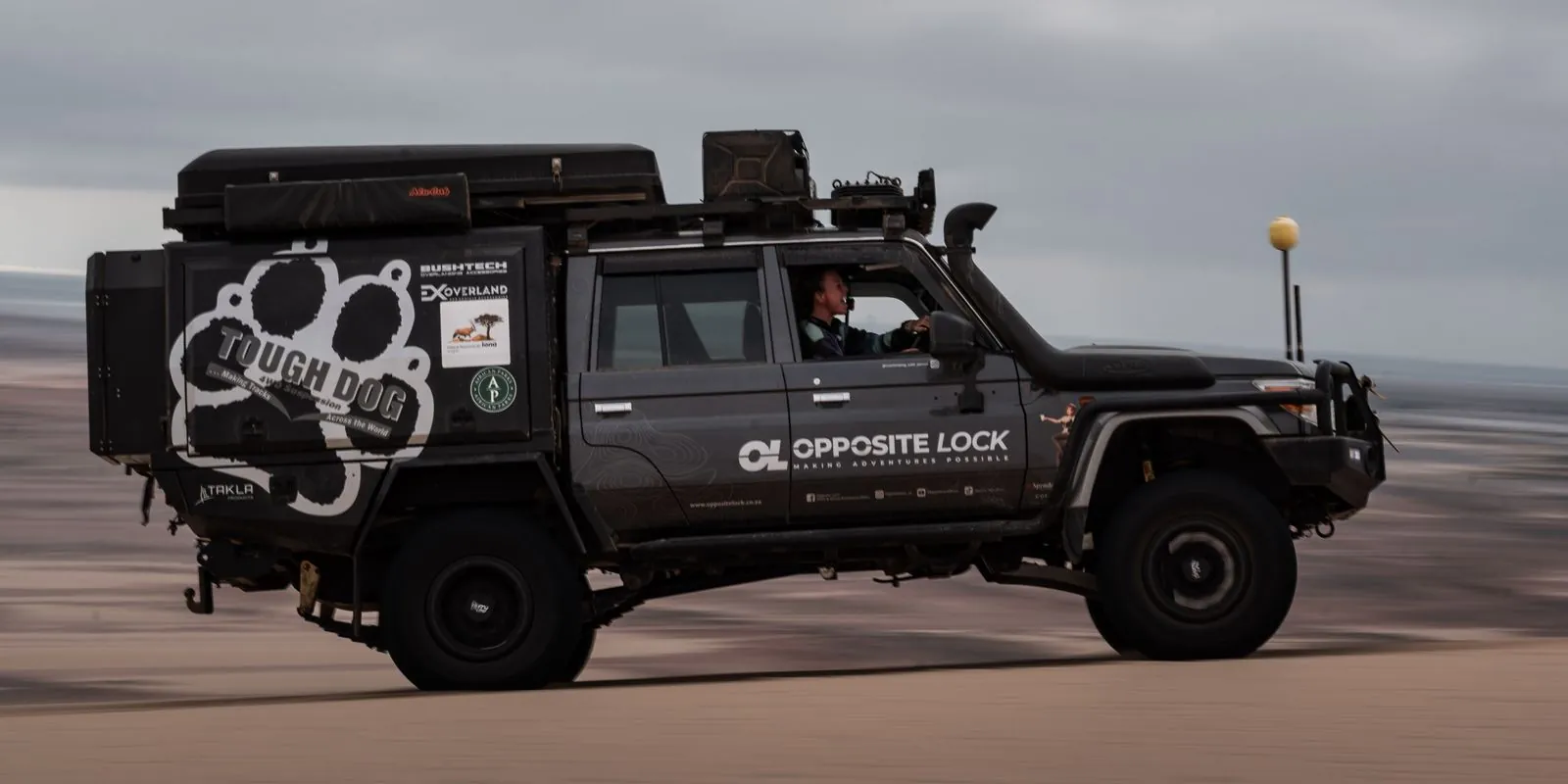 The Opposite Lock Land Cruiser 79 in side profile on the beach, bull bar, snorkel, roof rack, rooftop tent and canopy