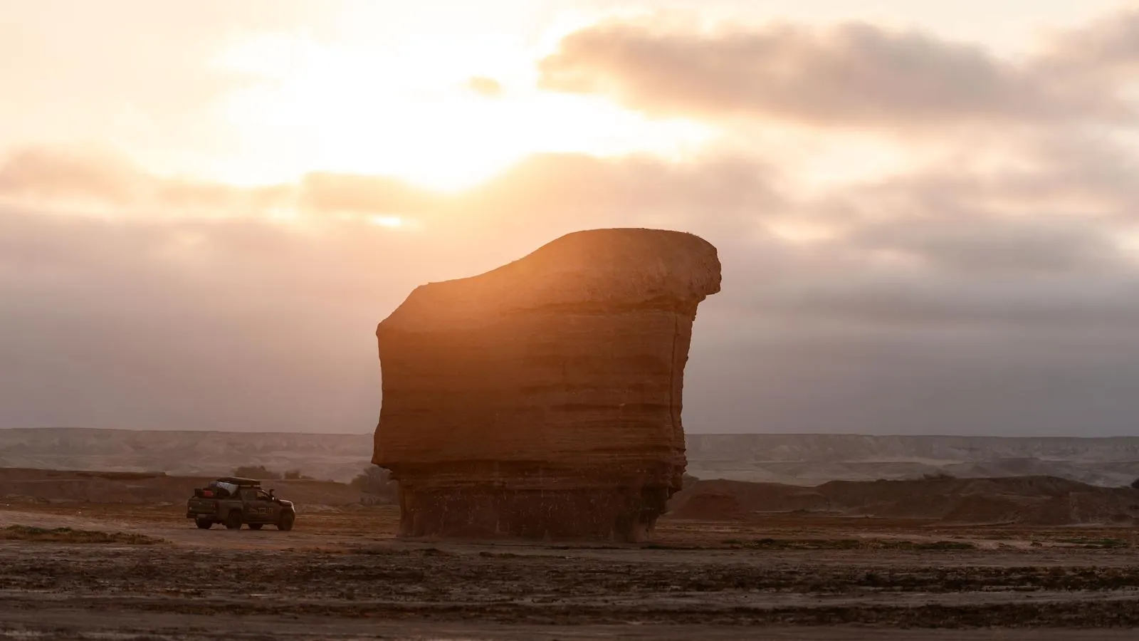A vehicle dwarfed by a rock formation at sunset, southern Angola