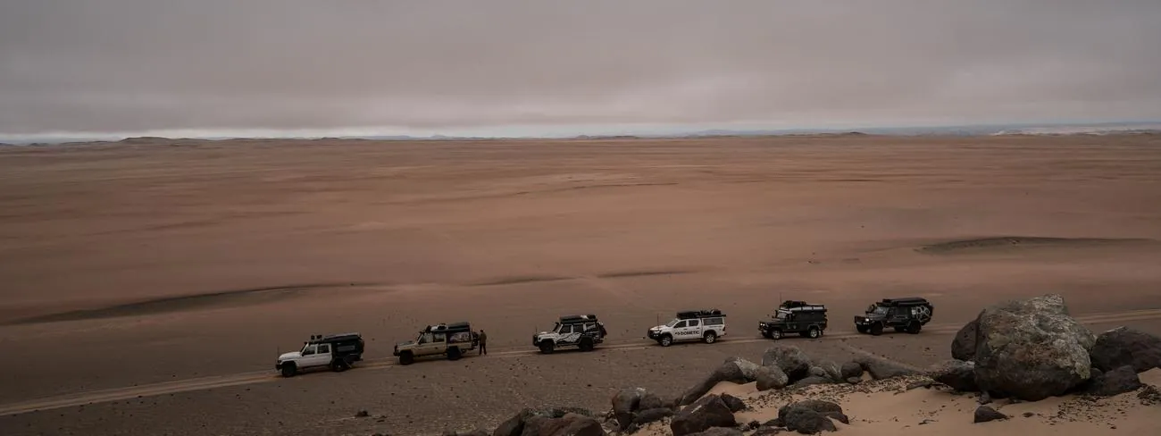 The convoy small against a wide beach and rock field