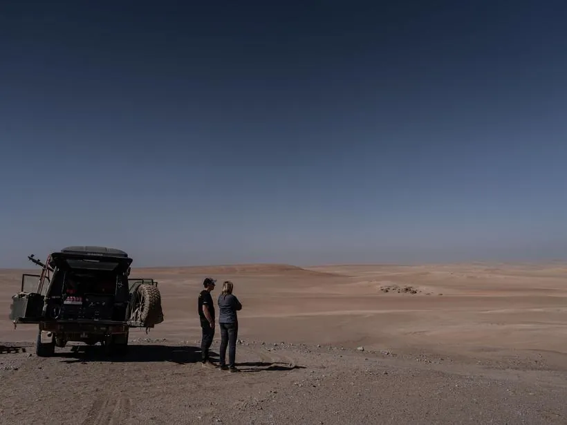 Two of the crew standing in open desert beside a vehicle