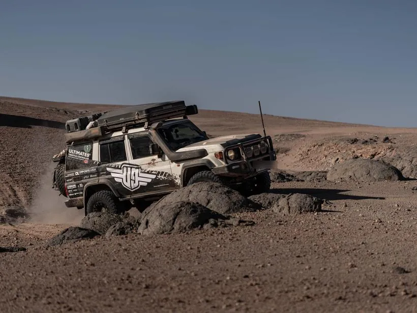 A Land Cruiser 76 climbing over black rock in open desert