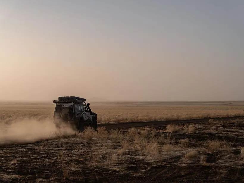 A vehicle trailing dust across open ground